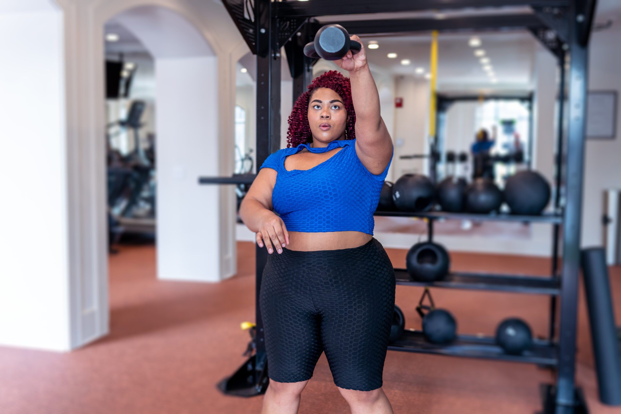 A multiracial woman does one armed kettlebell swings during a functional fitness workout at the gym.